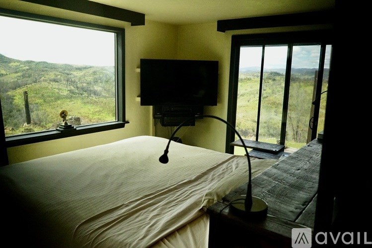 A bedroom with a bed, a television, and a window overlooking a landscape.