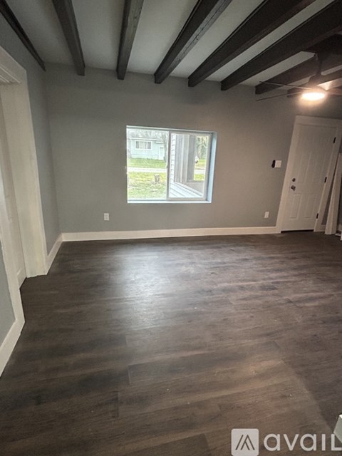 A room with wooden floors and a window showing a view of a house.