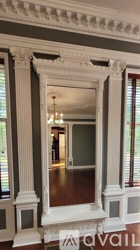 A large mirror with white trim and a chandelier is reflected in the mirror.