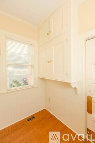 A room with white walls and wooden floors, with a window and a door visible.
