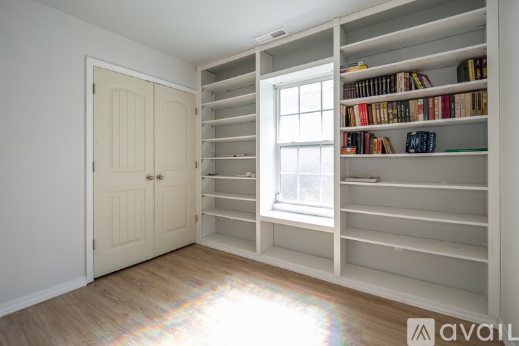 A room with a white door and a window with a bookshelf on the side.