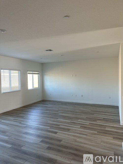 A spacious room with wooden flooring and two windows.