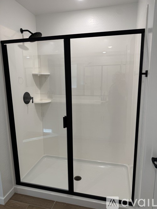 A glass shower stall with a black frame and a black handle.