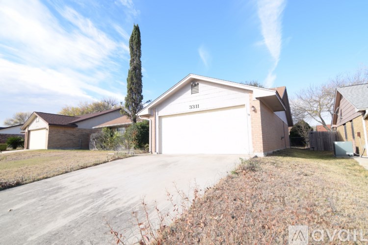 A house with the number 3311 on it is surrounded by a driveway and a tall tree.