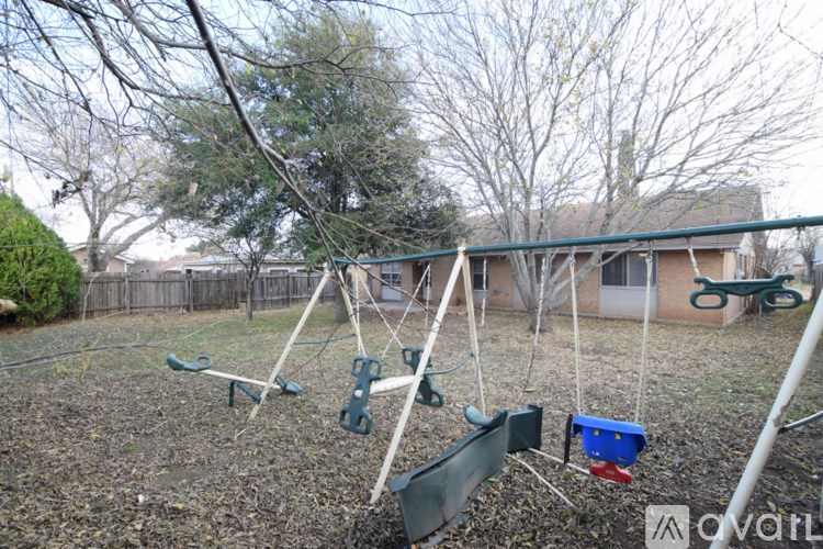 A playground with swings and a blue bucket on the ground.