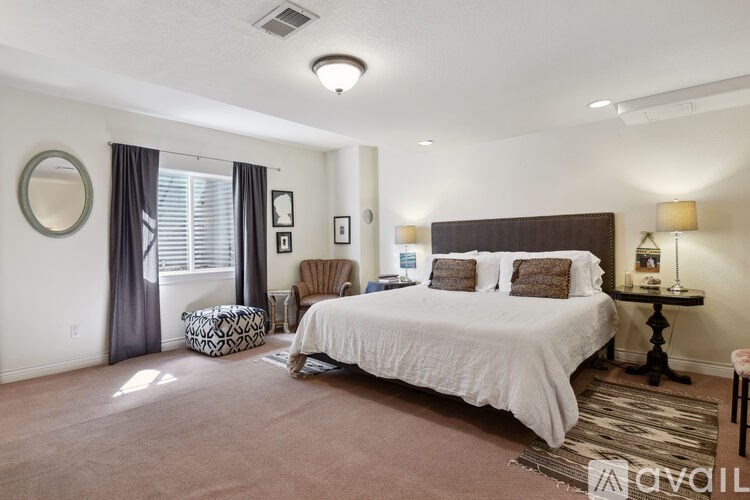 A bedroom with a large bed, a chair, and a round mirror on the wall.