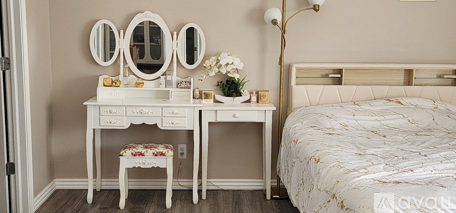 A white vanity table with a mirror and a small stool sits next to a bed in a bedroom.