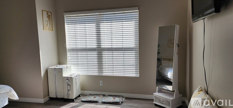 A room with a window covered by blinds and a TV mounted on the wall.