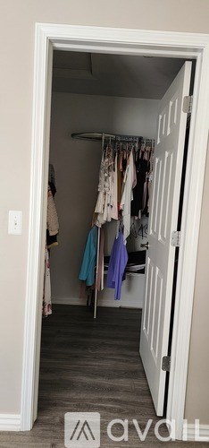 A white door is open to a room with a clothes rack and clothes hanging on it.