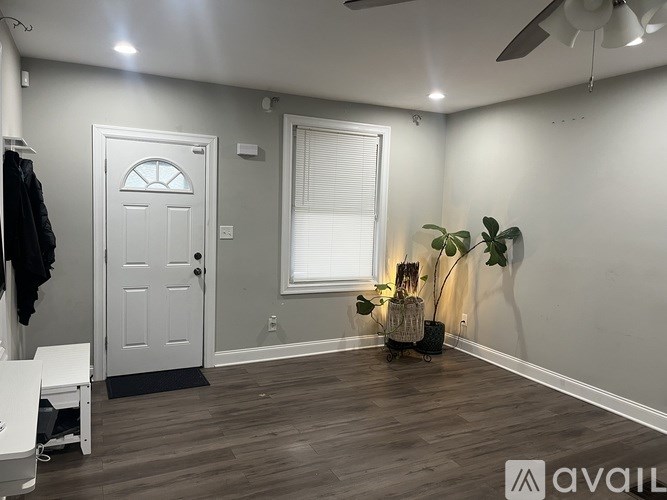 A room with a white door, a window with blinds, a ceiling fan, and a wooden floor.