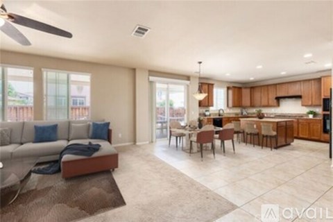 A spacious living room with a grey sofa and a kitchen area in the background.