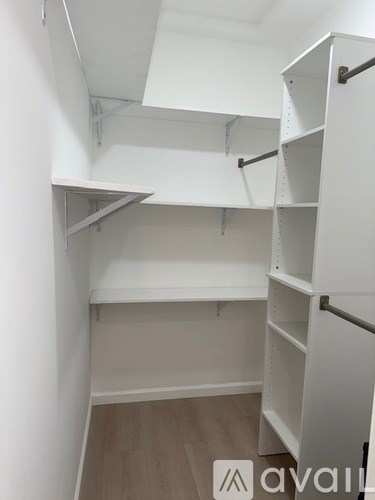 A white shelving unit with multiple shelves is installed in a room with wooden flooring.
