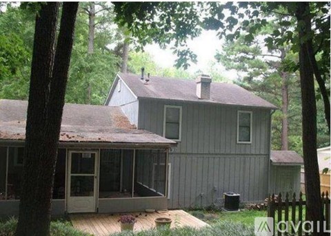 A house with a grey siding and a brown roof is surrounded by trees.