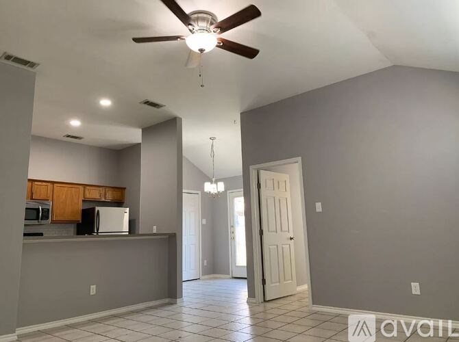 A spacious room with a ceiling fan and a kitchen area with wooden cabinets.