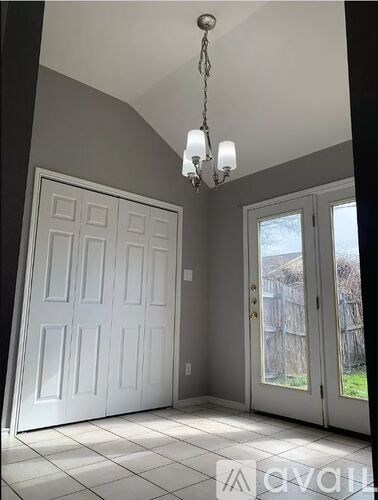 A chandelier hangs over a white door in a room with tiled flooring.