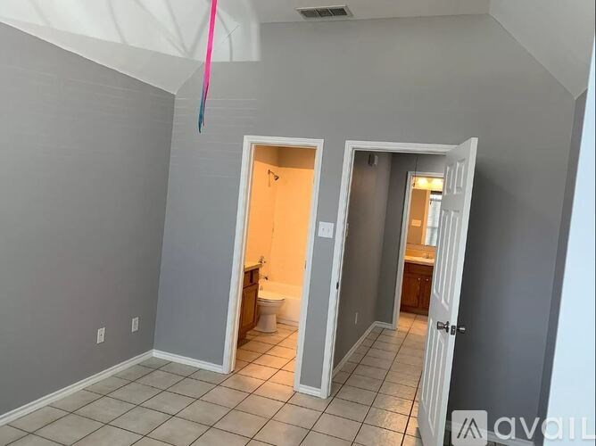 A room with a white door and a bathroom visible through the doorway.