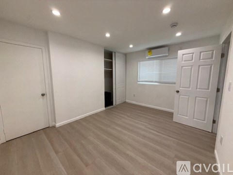 A spacious room with light wood flooring and white walls.