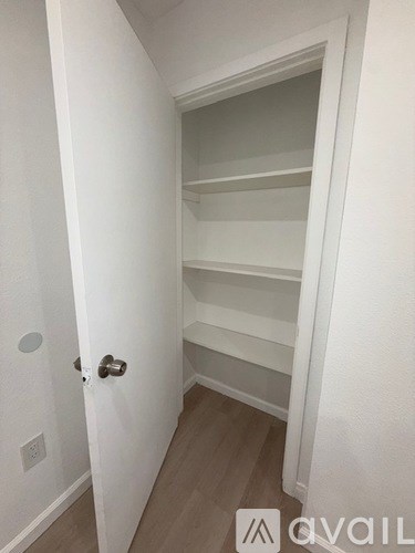 A white door with a handle is open to a hallway with a white wall and a light switch.