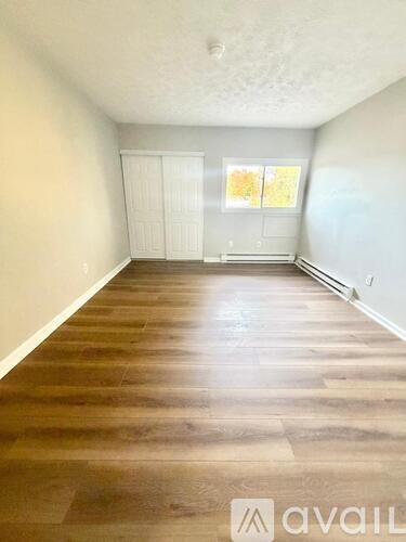 A room with wooden flooring and white walls, with a window on the right side.