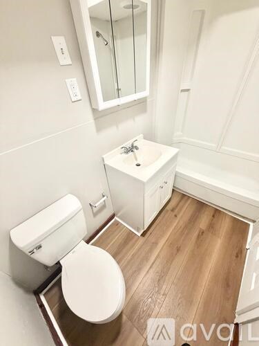 A white toilet sits in a bathroom with wood flooring and a white sink.