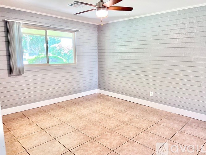 A room with a ceiling fan and a window with a view of trees.