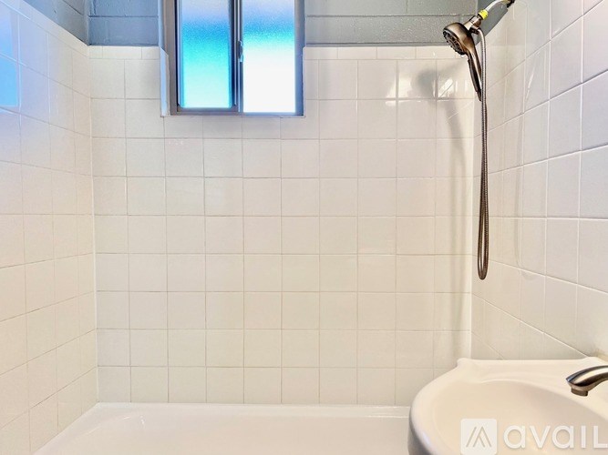 A white tiled bathroom with a shower head and tub.