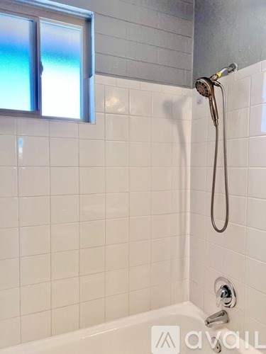A white tiled bathroom with a window and a shower.