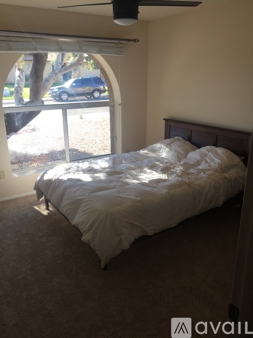 A bedroom with a bed, carpeted floor, and a window with a view of a tree and a car outside.