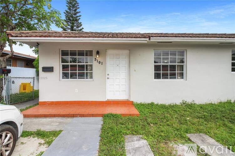 A small white house with a red door mat in front.