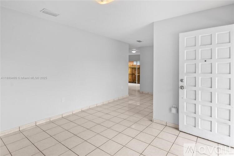 A white tiled room with a white door and a window in the distance.