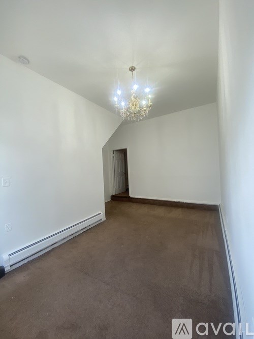A chandelier hangs from the ceiling in a room with white walls and carpeted floor.
