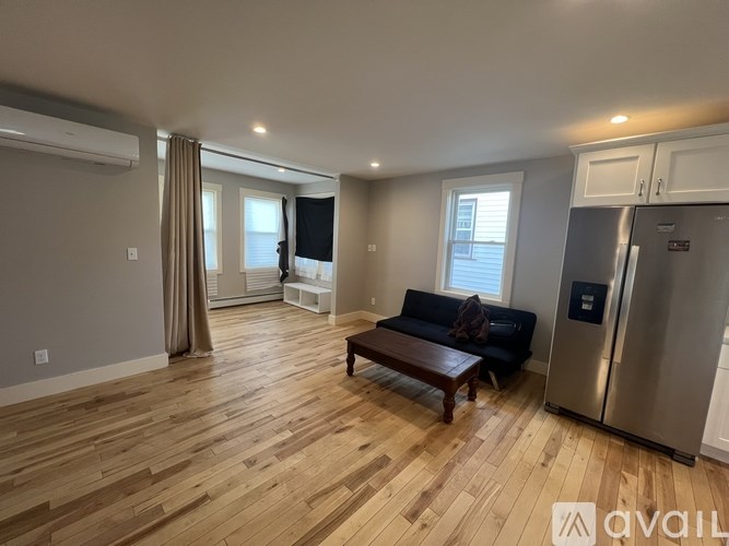 A kitchen with a refrigerator, cabinets, and a dining table in a room with wooden flooring.