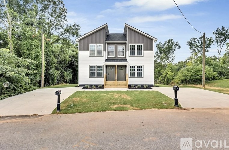 A two-story house with a grey and white exterior is surrounded by greenery.