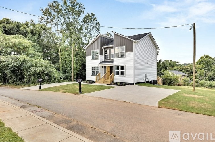 A two-story house with a grey exterior and a white trim is surrounded by greenery.