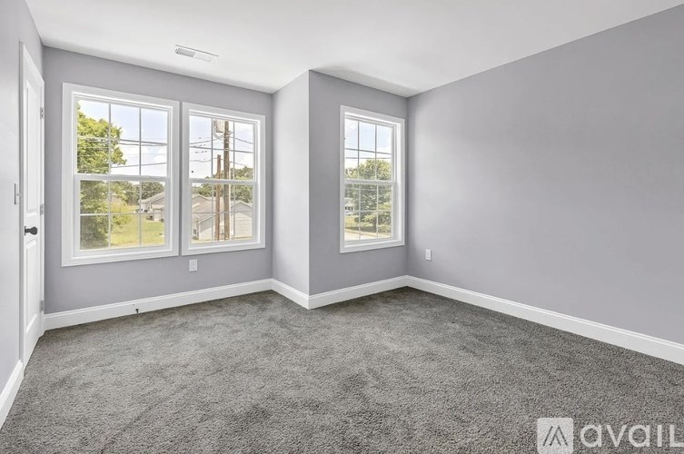 A room with grey carpet and two windows overlooking a street.
