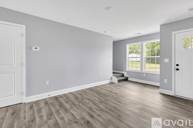 A room with wooden flooring and white walls, with a window showing daylight.
