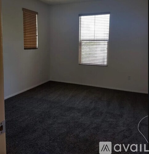 A room with a carpeted floor, a window with blinds, and a wall with a small hole.