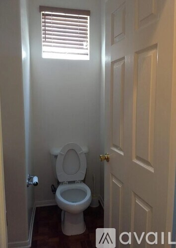 A white toilet in a small bathroom with a window above it.