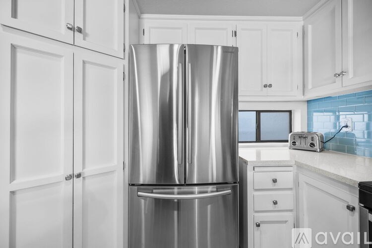 A stainless steel refrigerator stands in a kitchen with white cabinets.