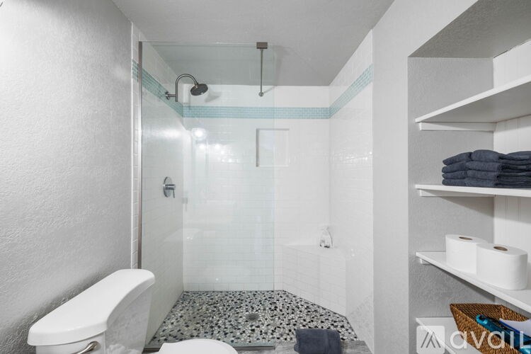 A bathroom with a toilet, a shower with a glass door, and a shelf with towels.