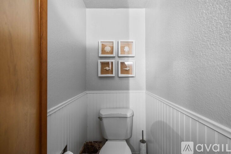 A white toilet in a small bathroom with a wooden door and three picture frames on the wall.