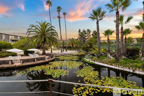 A serene pond surrounded by palm trees and lush greenery under a vibrant sky.
