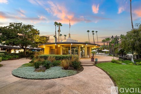 A building with a flag on top is surrounded by palm trees and has a circular garden in front.