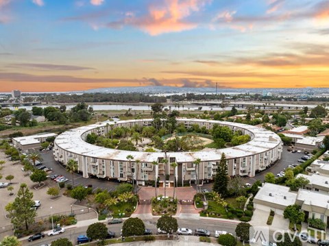 A large, circular building with a white roof is surrounded by trees and parking lots.
