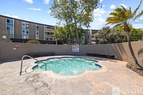 A small pool with a metal railing and a palm tree in front of a building.