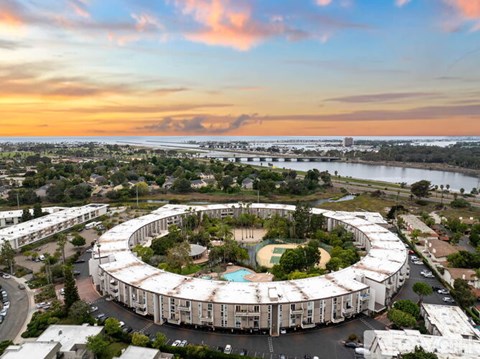 A large, circular building with a pool in the middle is surrounded by trees and is located in a residential area.