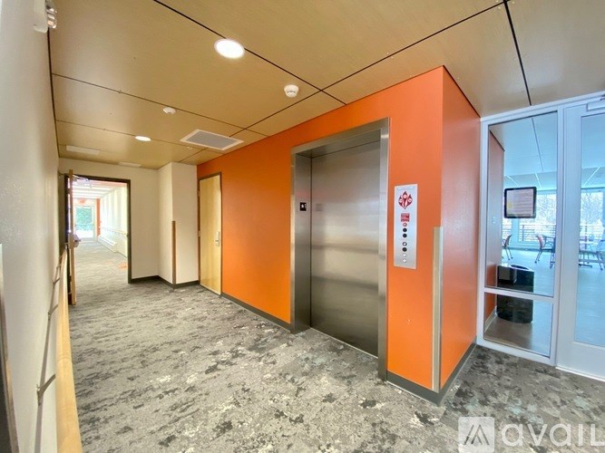 A hallway with a red wall and a silver elevator.