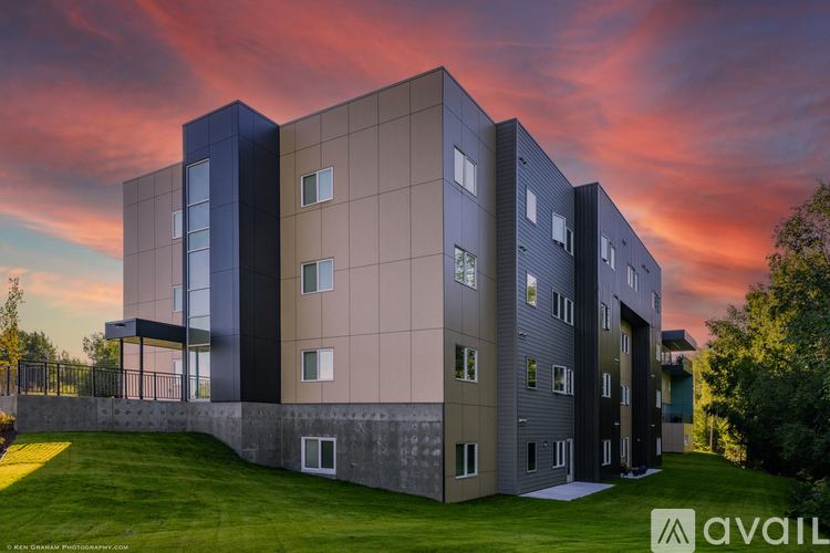 A modern building with a grassy area in front and a sunset sky in the background.