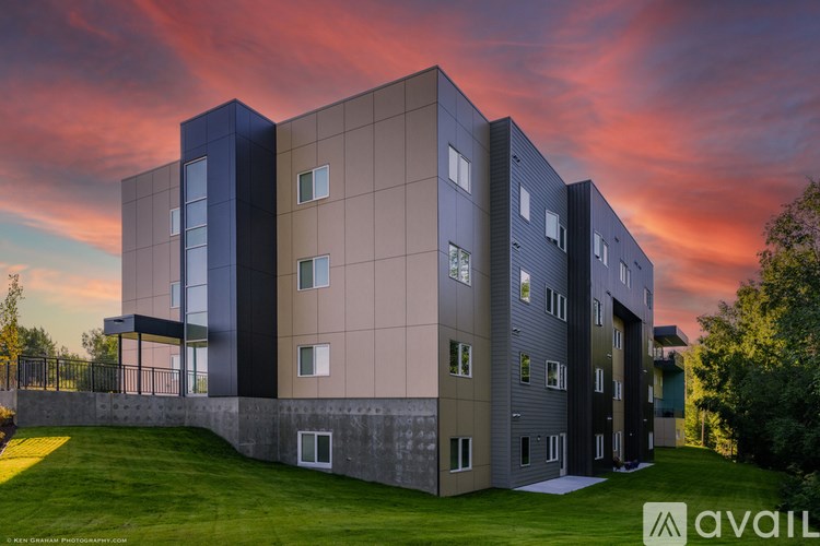 A modern building with a grassy area in front and a sunset sky in the background.