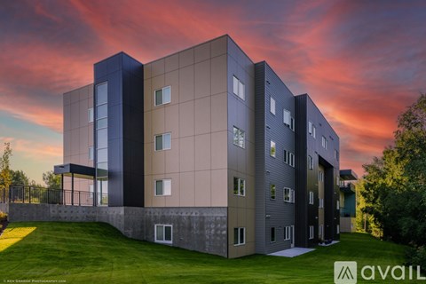 A modern building with a grassy area in front and a sunset sky in the background.